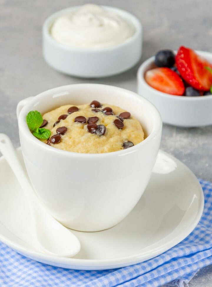 chocolate chip mug cake in a white cup and white spoon next to it