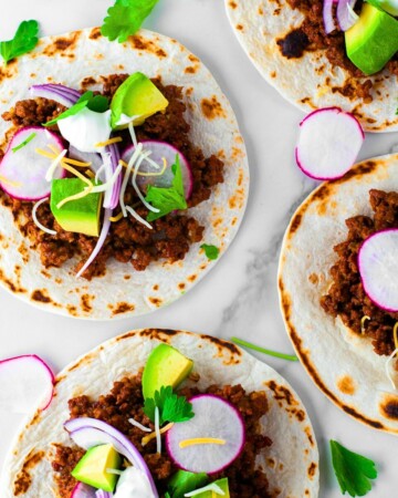 ground beef taco meat on multiple flour tortillas with avocado, onion and radish